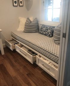 a white daybed with drawers underneath it in a small room next to a window