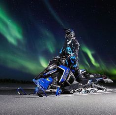 a man riding on the back of a snowmobile under an aurora bore in the sky