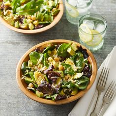 two wooden bowls filled with salad next to silverware and glasses on top of a table