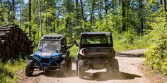 two vehicles driving down a dirt road in the woods