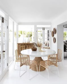 a white dining room with wicker chairs and a round table in the center surrounded by glass doors