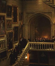 a group of people standing on top of a staircase in a room filled with paintings