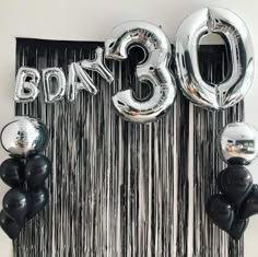 balloons and streamers in the shape of numbers are hanging on a wall next to a curtain