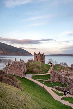 an old castle sitting on top of a lush green hillside next to a body of water