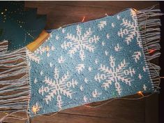 a blue knitted blanket with white snowflakes on it next to some christmas lights