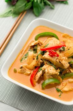 a white plate topped with chicken and veggies next to chopsticks on a table