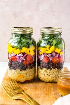 two mason jars filled with different types of salads and dressing on a cutting board