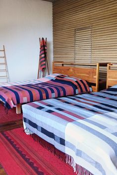 two beds in a room with red rugs and wooden slats on the wall