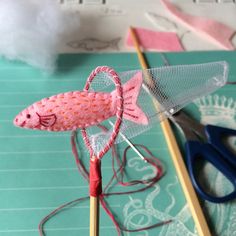 a pink knitted fish sitting on top of a table next to scissors and thread