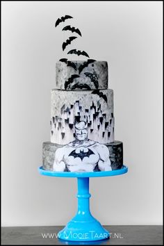 a three tiered cake decorated with black and white batman images is on a blue pedestal