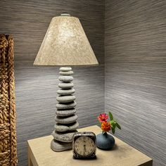 a lamp and some rocks on a table with a flower in a vase next to it