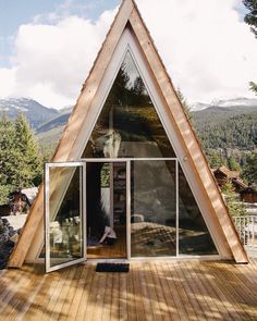 a house made out of wood and glass on top of a wooden deck with mountains in the background