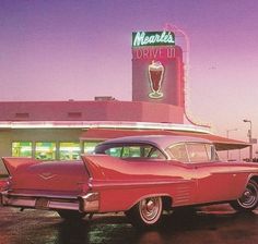 an old red car is parked in front of a drive - in restaurant with a tall neon sign