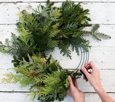 someone is making a wreath out of branches and evergreens on a white wooden surface