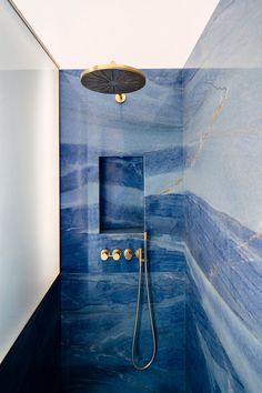 a bathroom with blue marble walls and floor, shower head and hand held faucet