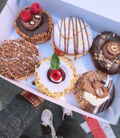 a box filled with assorted donuts on top of a table next to someone's feet