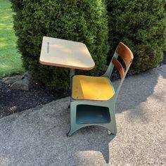 an old school desk and chair sitting in front of some bushes on the side walk