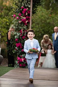 a young boy in a blue suit walking down the aisle with flowers on either side