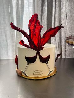 a white cake with red frosting and two wine glasses on top, sitting on a table