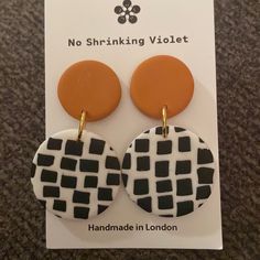 the earrings are black and white with an orange circle on it, sitting on a card that says no shrinking violett