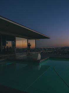 people are standing on the edge of a swimming pool at night with city lights in the background