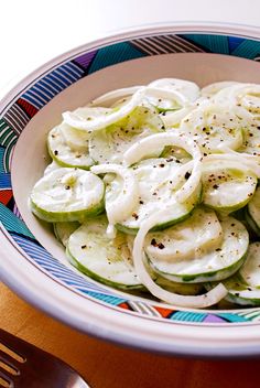 a bowl filled with sliced cucumbers on top of a wooden table next to a fork