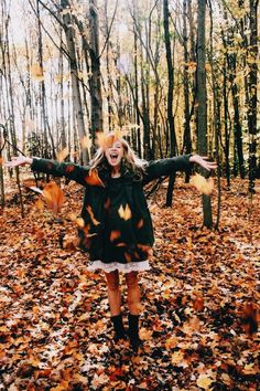 a woman is standing in the leaves with her arms spread out and eyes open, surrounded by trees