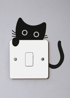 a black cat sitting on top of a white light switch cover with one eye open