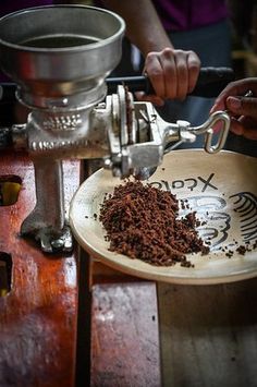 a person pouring coffee into a bowl on top of a wooden table next to a grinder