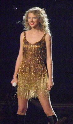 taylor swift performing on stage wearing a gold sequin dress and black knee high boots