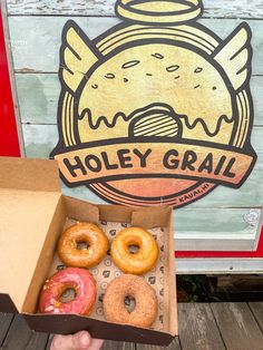 a person holding two donuts in front of a sign that says holey grail