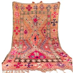 an orange and pink rug with fringes on the bottom, in front of a white background