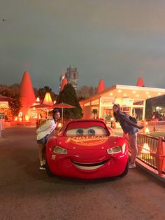 two people standing next to a red car