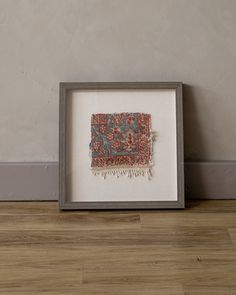 an old rug is displayed in a frame on the floor next to a wood floor