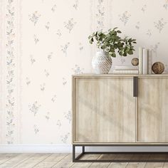 a vase with flowers on top of a wooden cabinet in front of a wallpapered background