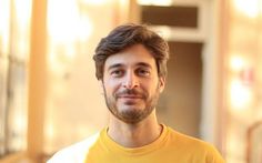 a man in a yellow shirt is looking at the camera while he stands near a building