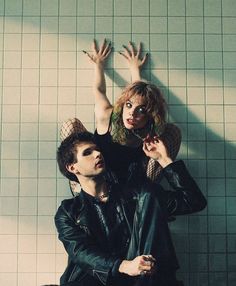 two people standing next to each other in front of a tiled wall with their hands up