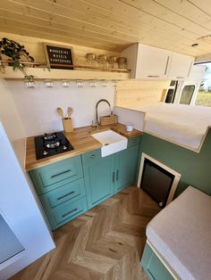 a small kitchen with a stove top oven and wooden flooring, along with a bed in the corner