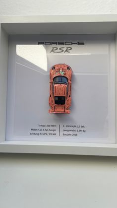 an orange sports car on display in a white frame with the porsche logo above it