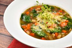 a white bowl filled with vegetable soup on top of a red cloth covered tablecloth