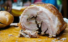 a large piece of meat sitting on top of a wooden cutting board next to bread