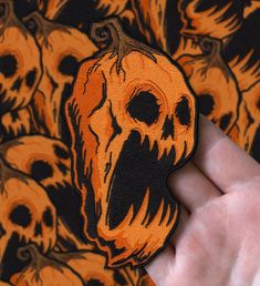 a hand is holding up a sticker with a skull on it and many other skulls in the background