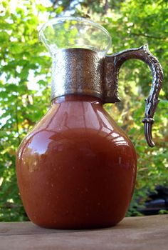 a brown jug with a handle sitting on top of a wooden table in front of some trees