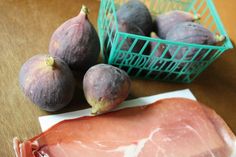 figs and ham on a table next to a green basket