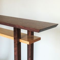 a wooden table sitting next to a white wall with a shelf underneath it on the floor