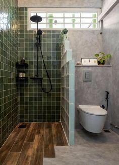 a bathroom with green tile and wooden flooring next to a toilet in the corner