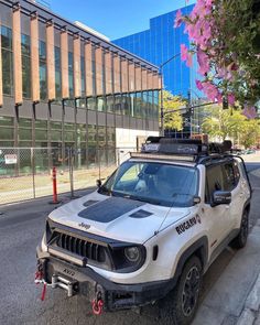 a white jeep parked on the side of a road next to a tall glass building