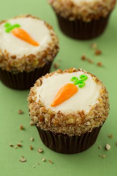 three cupcakes with frosting and carrots on them sitting on a green surface