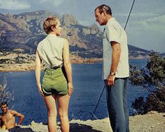 two men and a woman standing on top of a hill next to a body of water