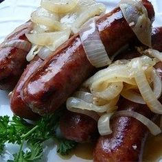 two sausages with onions and parmesan cheese on a white plate next to some parsley